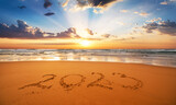 Fototapeta Mapy - Happy New Year 2023 concept, lettering on the beach. Written text on the sea beach at sunrise.