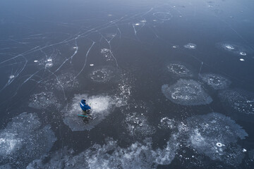 Wall Mural - Frozen pond with ice flowers made of ice crystals. A lone fisherman is sitting at the hole with a fishing rod in his hand. There is an ice drill nearby. Shooting from a drone.