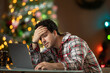 © SuperStock - Young man stressed out with hand on forehead online shopping in front of a Christmas Tree