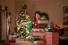 Young woman holding Christmas gifts in front of a Christmas Tree in her living room. 
