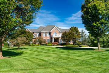 large modern brick house with colonial style balcony. single family home with large mowed lawn and b