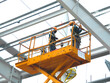 © Hor - Workers install lighting fixture in a hug industrial warehouse using hydraulic scissor lift. MEP work in construction site.