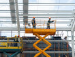 © Hor - Workers install lighting fixture in a hug industrial warehouse using hydraulic scissor lift. MEP work in construction site.
