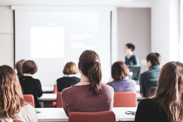 Wall Mural - female speaker giving presentation in lecture hall at university workshop . participants listening t
