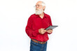 Serious senior man using tablet computer. Confident Caucasian male model with gray hair and beard in red shirt and glasses looking away at ad, browsing web. Modern technology, advertising concept