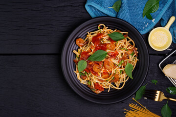 Canvas Print - Delicious spaghetti pasta with prawns and cheese served on a black plate on a black background table Italian recipe, tomato sauce, vegetables, and spices top view with copy space