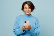 © ViDi Studio - Young smiling happy fun caucasian woman wear knitted sweater hold in hand use mobile cell phone chatting isolated on plain pastel light blue cyan background studio portrait. People lifestyle concept.