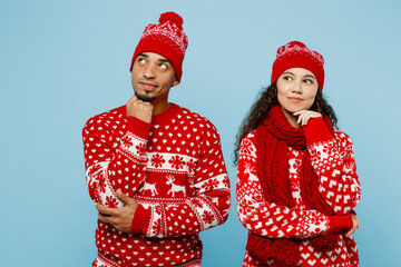 Wall Mural - Merry young couple friends two man woman wear red Christmas sweater Santa hat posing prop up chin look aside on area isolated on plain pastel light blue background Happy New Year 2023 holiday concept