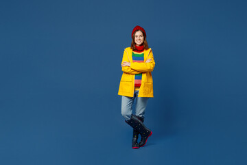 Full body fun young woman wear sweater red hat yellow waterproof raincoat outerwear hold hands crossed folded isolated on plain dark royal navy blue background Outdoor wet fall weather season concept