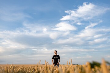 a man stands in a wheat field against a background of a blue sky with textured clouds