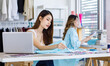 © Bangkok Click Studio - Millennial Asian young beautiful female designer dressmaker sitting at working table using measuring tape measure fabric while colleague sew clothing with sewing machine in studio office workshop