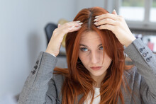 Young Businesswoman With Dyed Red Hair Checking Her Root Regrowth In The Mirror