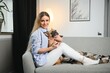 © Serhii - Young pretty woman in casual clothes hugging her dog sitting on the sofa in the living room of her cozy country house. Animal communication concept
