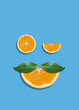 Creative summer face with eyes made of orange fruit slices and mustache made of leaves on bright blue vibrant background. Orange juice minimal tropic concept. Winking eye funny idea