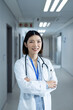 © wavebreak3 - Vertical portrait of smiling asian female doctor in hospital corridor, copy space
