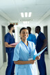 © WavebreakMediaMicro - Vertical portrait of smiling biracial female healthcare worker in busy hospital corridor, copy space