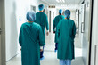 Rear view of four surgeons in surgical caps and gowns walking in hospital corridor