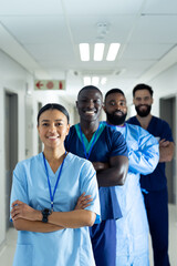 Vertical portrait of diverse group of smiling healthcare workers in line in corridor, copy space