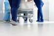 Low section of healthcare workers pushing patient in bed down hospital corridor, with copy space