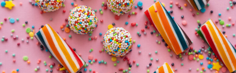 Wall Mural - Top view of delicious sweets and sprinkles on pink background, banner.