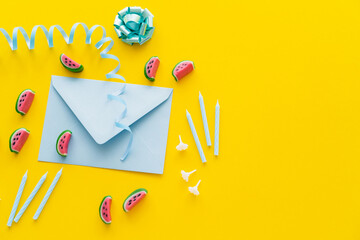 Top view of festive candles near envelope and sweets on yellow background.