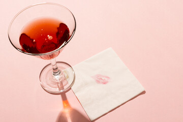 Poster - Red cocktail in glass, with lipstick print on napkin, on pale pink background with copy space
