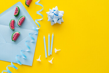 Wall Mural - Top view of candies on envelope near festive candles and serpentine on yellow background.