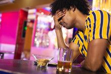 Depressed African American Man Sitting At The Bar With A Beer And Holding His Head
