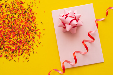 Wall Mural - top view of pink greeting card with gift bow and blurred sprinkles on yellow background.