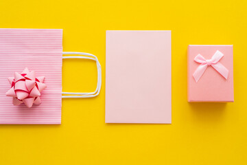 Wall Mural - top view of pink gift near empty greeting card and shopping bag on yellow background.