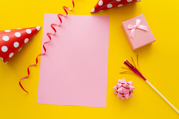 Wall Mural - top view of empty greeting card near dotted party caps and gift box on yellow background.