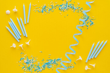 Wall Mural - Top view of candles near blue serpentine and sprinkles on yellow background.