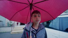 One Young Boy Walking Outside Holding Red Umbrella While Raining. Adolescent Kid Walks Outdoors During Rainy Day