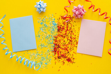 Wall Mural - top view of blue and pink greeting cards near sprinkles and serpentine on yellow background.