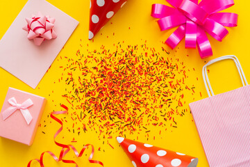 Wall Mural - top view of festive gift near party caps and sprinkles on yellow background.