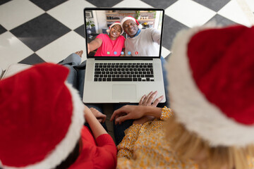 Wall Mural - Caucasian mother and daughter having christmas video call with senior african american couple