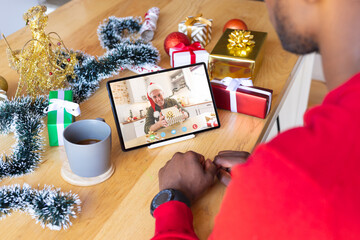 Wall Mural - African american man with christmas decorations having video call with happy caucasian man