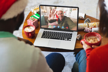 Wall Mural - Diverse couple with christmas decorations having video call with happy caucasian man