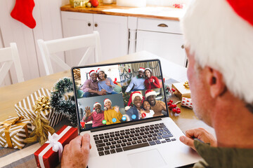 Wall Mural - Caucasian man with santa hat having video call with happy diverse friends