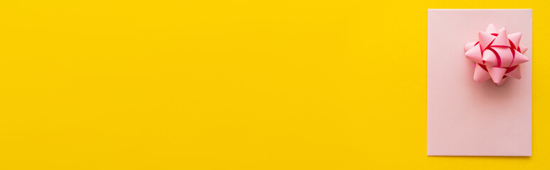 Wall Mural - top view of pink greeting card and gift bow on yellow background, banner.