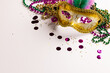 Composition of colourful mardi gras beads and carnival mask on white background with copy space