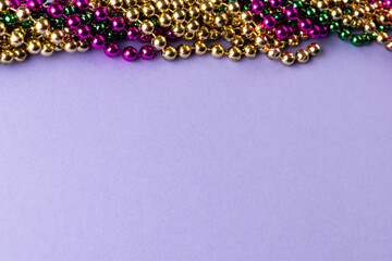 Wall Mural - composition of colourful mardi gras beads on lilac background with copy space