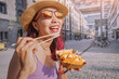 Happy cheerful girl eating spring rolls from takeaway paper box using chopsticks at Cologne city street. Fast food eatery and asian cuisine