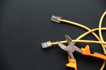 pliers and yellow internet cable on a black background. the concept of turning off wired internet for non-payment.