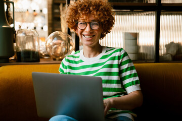 Cheerful middle-aged woman in eyeglasses using laptop while sitting in cafe