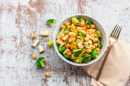 Healthy food broccoli salad add apple chickpeas in white bowl on wood background.