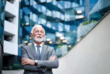 Thoughtful elderly entrepreneur standing with arms crossed outside business office building.