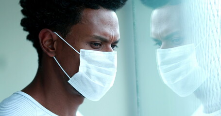 African man wearing covid coronavius face mask at home looking out window indoors