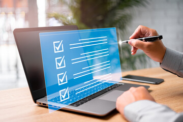 Digital work checklist on virtual screen concept, Businessman use a pen point on checklist and use laptop working in office Document Management System and process automation to efficiently manage file