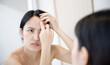 Problem skin. Concerned young asian women popping pimple on cheek while standing near mirror in bathroom. young asian women with acne